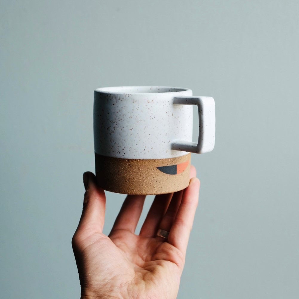 A handmade ceramic mug with a square handle and a black and red gemoetric pattern applied as an undergalze