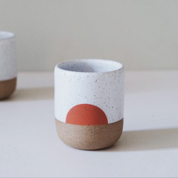 A handmade cup with a half-circle design in orange.