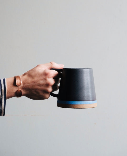 Black mug with blue stripe in a hand
