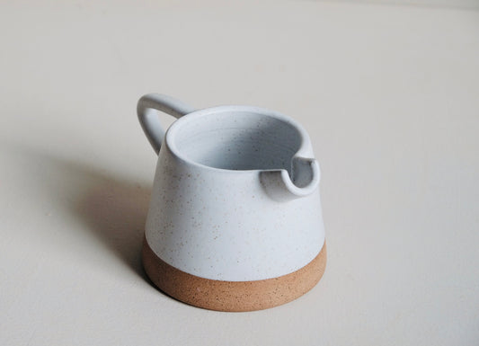 Ceramic pitcher with a speckled gray body and brown base on a light background