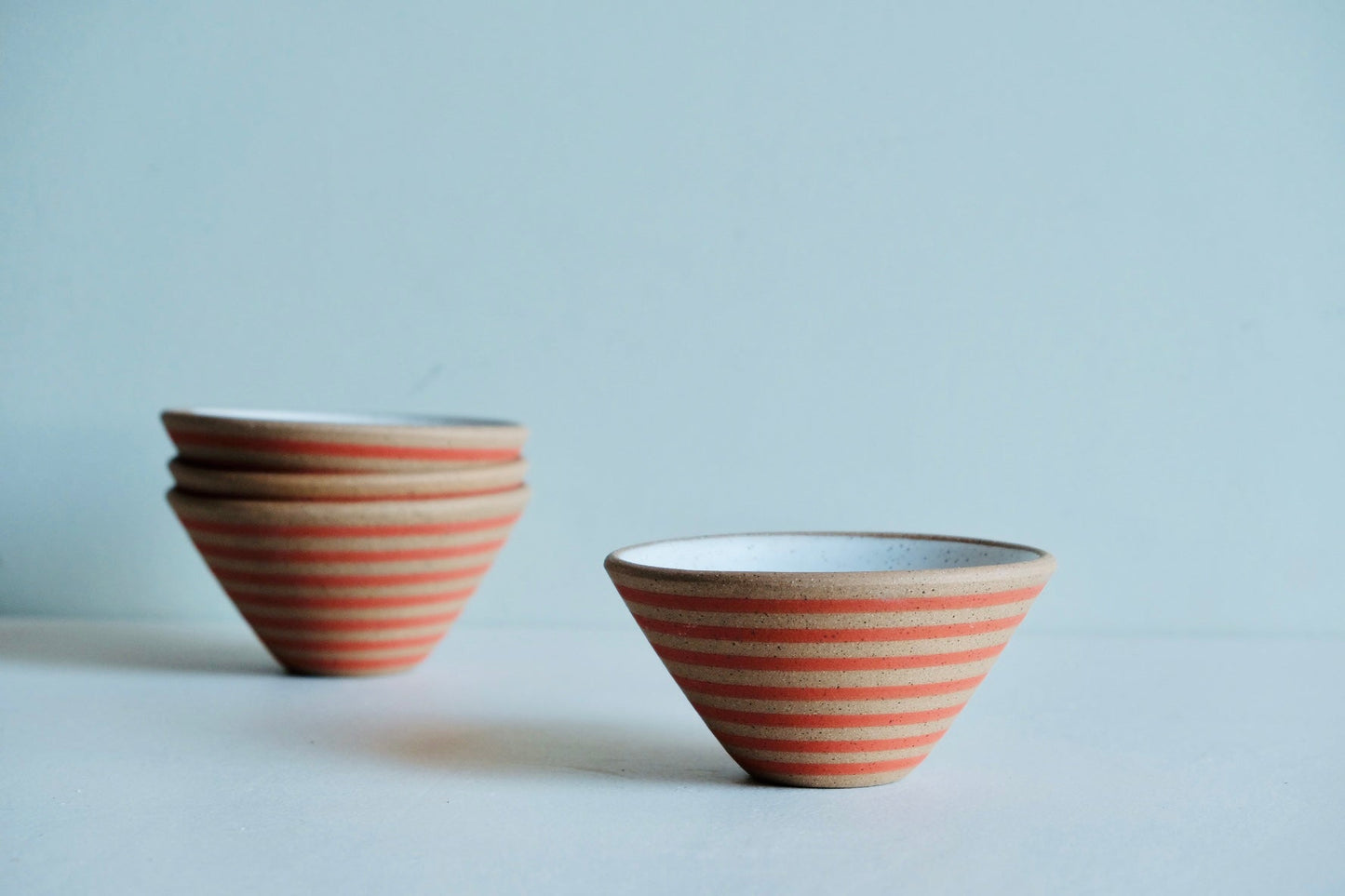 A bowl 3/4 dipped in white satin glaze with cute stripes of red at the bottom.